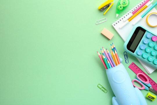 Rocket-shaped pencil case with school supplies, calculator, sharpeners, erasers, notepad, ruler on pastel green background. Back to school, education concept.