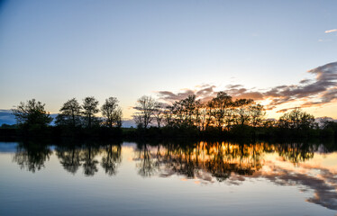 Fototapeta premium Serene sunset over a French river with calm waters reflecting clouds and shoreline trees
