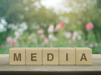 Media letter on wood block cubes on wooden table over blur pink flower and tree in garden, Business...