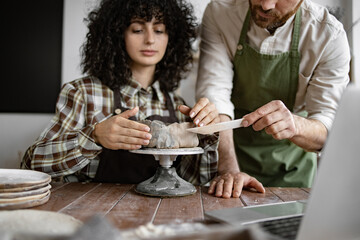 Man teaching woman pottery techniques at studio. Both concentrating on creating a clay sculpture.