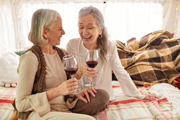 Two middle-aged women, a lesbian couple, enjoy a glass of wine while laughing together inside their camper van.