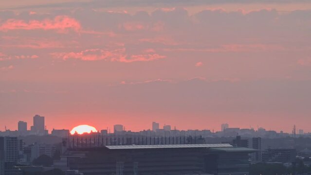 都市のビル群の向こうから昇る朝陽