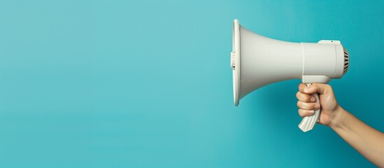 Male hand with a white hand-held loudspeaker on a blue background. Announcement and advertising at street markets and fairs. Copy space