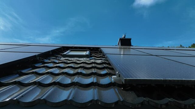 Low angle view looking up a solar panel array installed on metal roof of house, tracking right to left