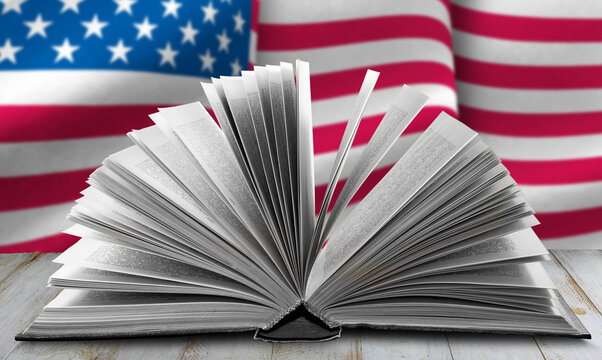 A close-up photo of an open book with its pages fanned out. The book is in focus, while the background is a blurred American flag.