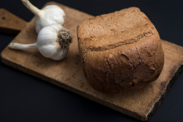 Brown bread and  garlic on a wooden table against a dark background.