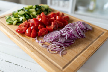 Fresh chopped vegetables such as cucumber, tomatoes and onions on a cutting bord in the kitchen