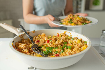 Fresh cooked healthy pan dish with couscous, chicken, beans and vegetables served by a woman with...