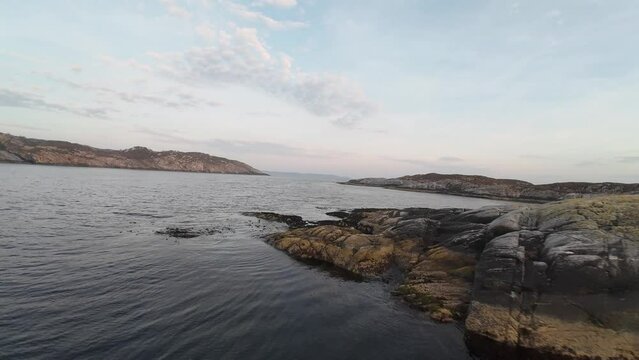 FPV aerial cruising at low altitude around coastal islands near Sotra and Bergen, Norway, close to the sea surface at sunset