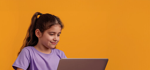 A young girl is sitting at a table with a laptop in front of her. She is smiling and she is enjoying her time on the computer. 12 yo girl in violet t-shirt coding on laptop, solid orange background
