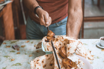 close-up view of person cooking delicious kebabs with fried bread.