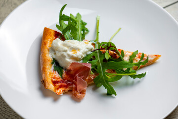 piece of pizza with smoked salmon and arugula on a white plate