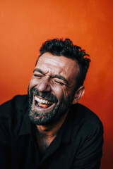 Obraz premium A man with a beard is laughing with his eyes closed against a bright orange backdrop