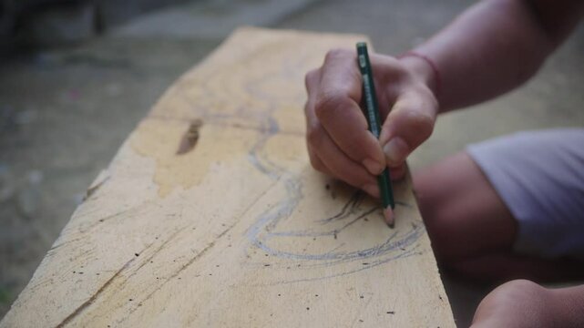 A close-up shot of a Balinese maskmaker's hands sketching the pattern for a traditional Balinese mask, known as Barang Bangkung, onto the sacred wood. Traditional woodcarver from Ubud, Bali. 