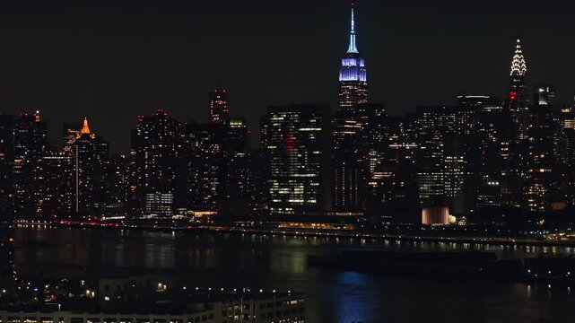 An aerial view at night over Long Island City, Queens with the Eastside of New York City in the background. The drone camera is stationary facing towards the East River and the city.