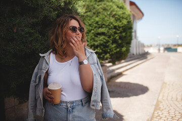 Plus size woman dressed jeans shirt, sunglasses, t-shert and skirt ealking in the street, Woman holding a cup of coffee.  The girl walking in windy day