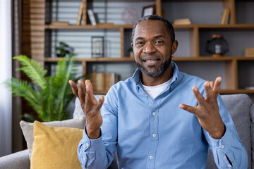 A man in a blue shirt having a lively conversation during a video call at home, showing engagement...