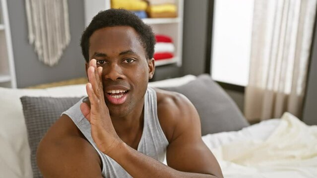 Gossip in pjs, young african american man spills secrets in hushed whisper, hand hiding mouth, engaged in malicious bedroom talk
