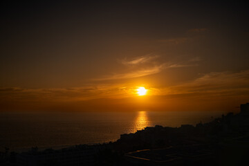 The sun is setting over the ocean, casting a warm glow over the water. The sky is filled with clouds, creating a serene and peaceful atmosphere