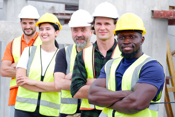 A team of male and female engineers stand smiling at a construction site for the housing industry.