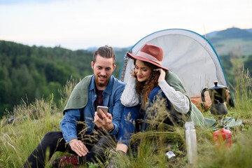 Travellers couple spending time outdoor, sleeping in tent shelter. Young tourist sitting in nature, taking selfie with smartphone. Summer vacation in nature.