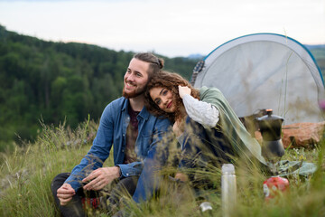 Travellers couple spending time outdoor, sleeping in tent shelter. Young tourist sitting in nature,...