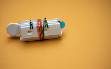 A bunch of Covid-19 test cassettes tied with rubber bands, with two people figurines sitting on the cassette; isolated on orange background. A close-up and selective focus photo of the cassette. 