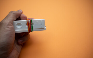 A left hand is holding a few of Covid-19 rapid antigen test cassettes (tied with colorful rubber...