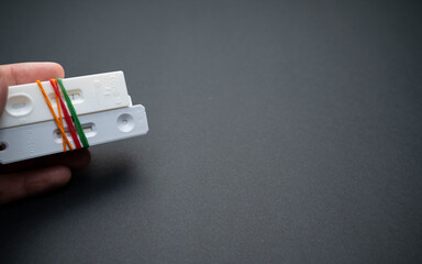 A left hand is holding a bunch of Covid-19 rapid antigen test cassettes tied with rubber bands;...