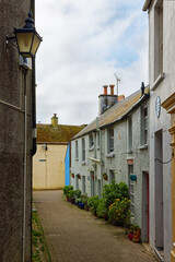 A narrow walkway past houses and flowers with a gas lamp on the wall in Tenby Wales UK