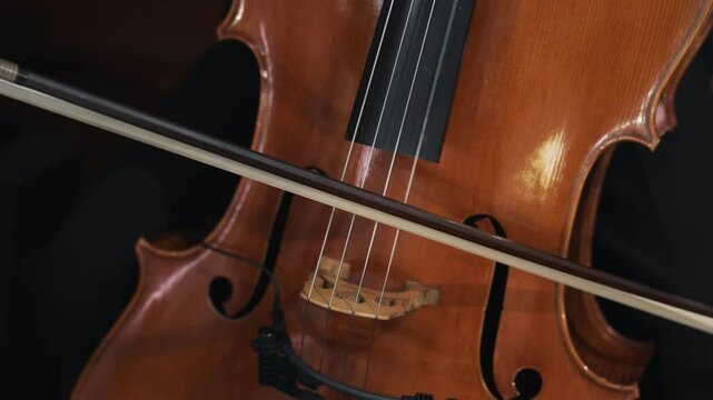 Close-up of a musician playing a cello with a bow, highlighting the strings and wooden body.