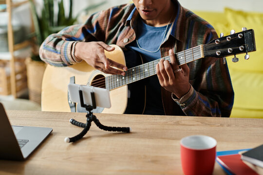 Young African American male blogger plays guitar while speaking on phone camera. - Powered by Adobe