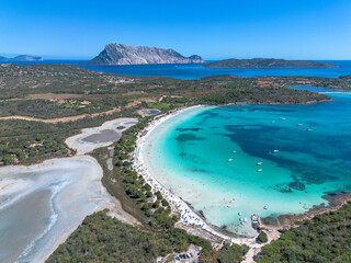 The splendid beach of Cala Brandinchi seen from the drone, with its white sand and the emerald blue sea, behind the beach a suggestive lake as well as the panorama with Tavolara in the background. San