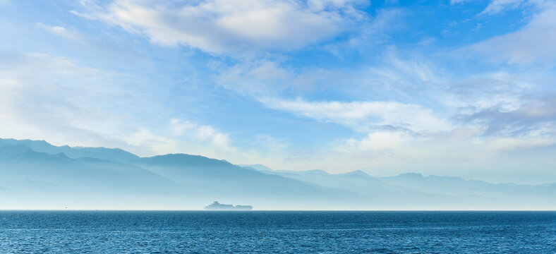 tropical seascape of sailing kargo tanker ship in sea with beautiful sunset and mountains on background