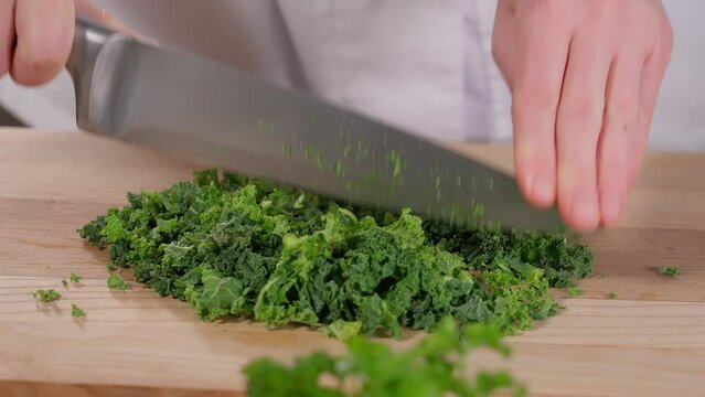 The chef uses a sharp knife to chop kale cabbage, herbs, and green salad on a wooden board. Prepares healthy breakfast, lunch, dinner, healthy eating concept, vegetables. Close-up, front view