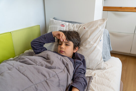 Boy feeling unwell lying in bed holding his head