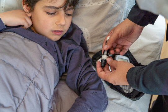 Anonymous mother checking hypoglycemic son's forehead in bedroom