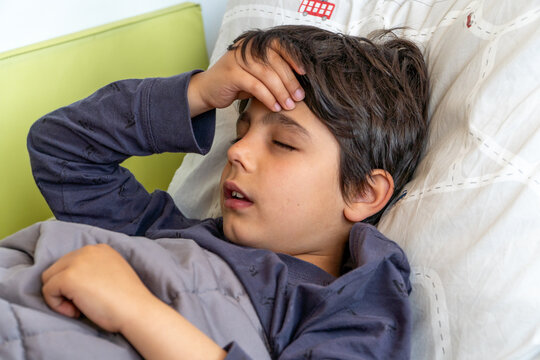 Boy feeling unwell lying in bed holding his head