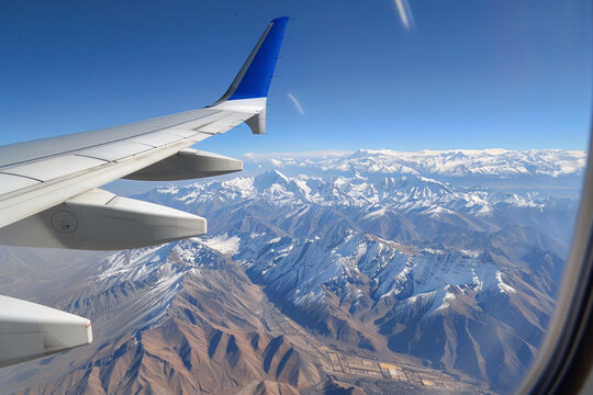 View from the window of flying airplane to the wing and snow-capped mountains