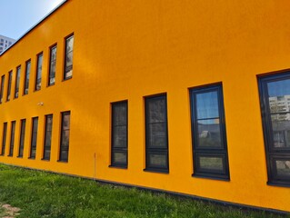 Orange wall and windows in black frames, green grass. Yellow concrete background with window