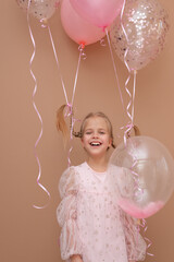 Happy beautiful blonde girl with pigtails in a pink dress with balloons on a brown background....