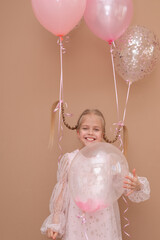 Fun beautiful blonde girl with pigtails in a pink dress with balloons on a brown background....