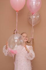 Beautiful blonde girl with pigtails in a dress with balloons on a brown background. Party concept....