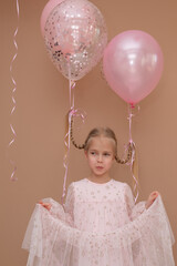 Girl in a pink dress and balloons lifting her pigtails up on a brown background. Vertical...
