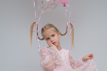 Beautiful girl with pigtails in a pink dress with balloons on a gray background.