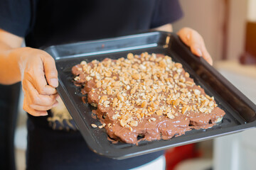 Close up of woman hands holding a baking sheet before take to the oven with cookies with chocolate.
