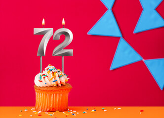 Number 72 candle with birthday cupcake on a red background with blue pennants