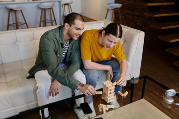 A young gay couple plays a game of blocks on a coffee table in their modern apartment.