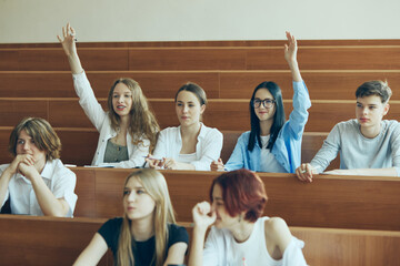 Involved students, girls raising hands to give answer during lecture. Students sitting in...