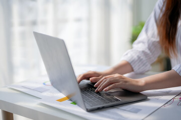 Close-up of person's hands typing on a laptop keyboard at a white desk with documents, showcasing productivity in a modern workspace.